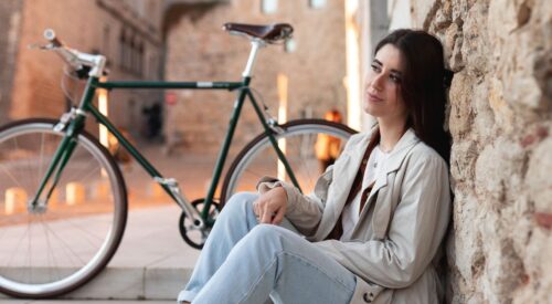 Femme assise en ville avec son vélo, prenant un moment pour elle, symbole de bien-être et de temps pour soi