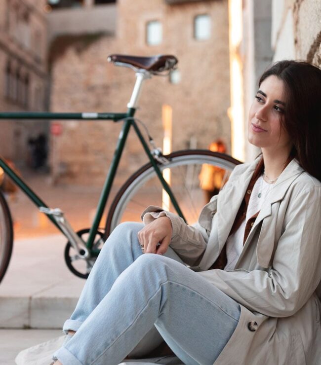 Femme assise en ville avec son vélo, prenant un moment pour elle, symbole de bien-être et de temps pour soi