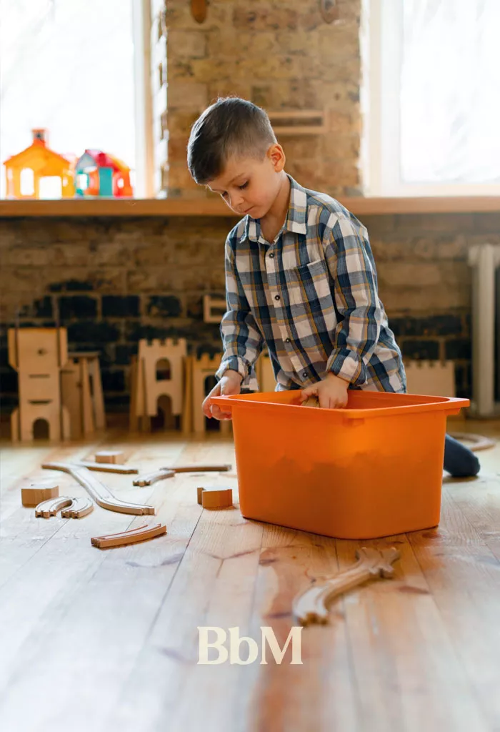 maison range enfant routine salle de jeux organisation.bebymaman Enfant rangeant seul ses jouets dans un grand bac de rangement après une séance de jeu, illustration de l'autonomie des enfants grâce à des rangements accessibles et adaptés à la maison.