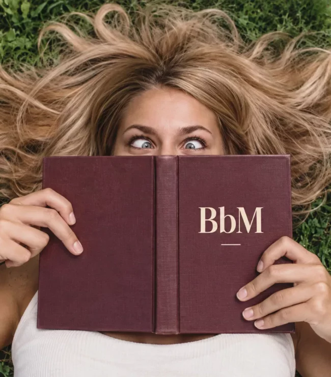 Femme allongée dans l’herbe derrière un livre BbM, les yeux louchant avec humour