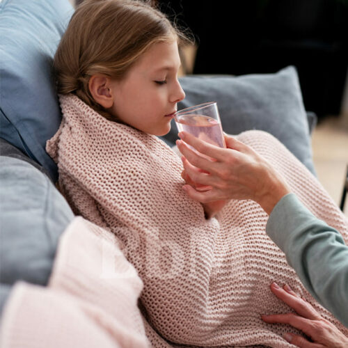 maman enfant malade charge mentale parentalite bebymaman Petite fille malade sous une couverture, réconfortée par sa maman qui lui tend un verre d’eau, illustration de la parentalité et des imprévus familiaux
