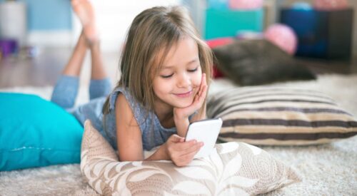 Petite fille allongée sur un tapis regardant son téléphone portable avec le sourire