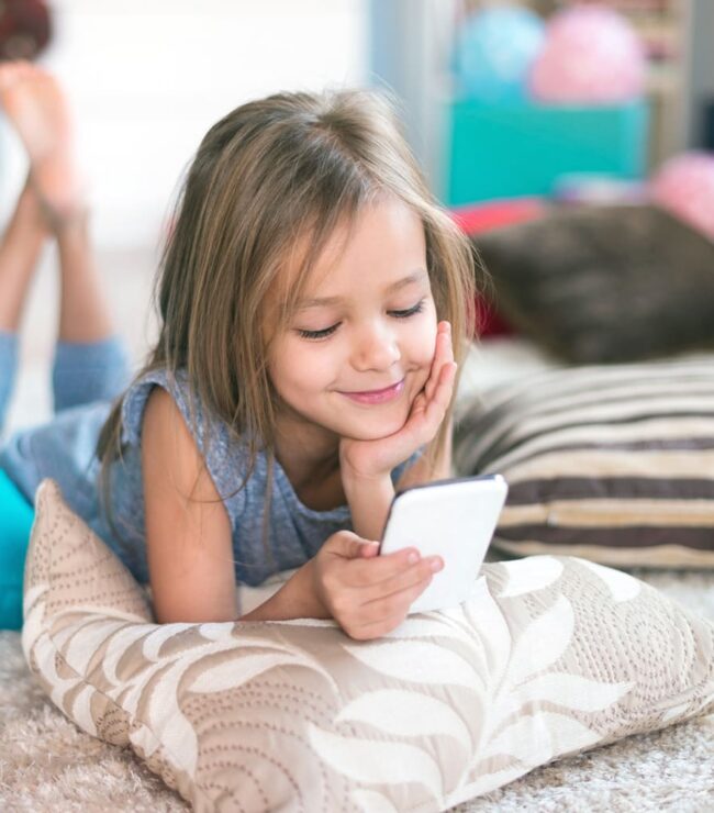 Petite fille allongée sur un tapis regardant son téléphone portable avec le sourire