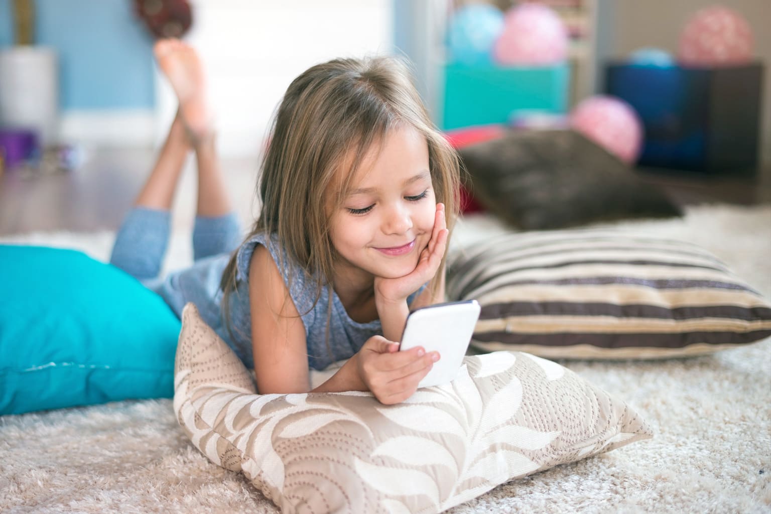 Petite fille souriante utilisant son premier téléphone portable à la maison – Be by Maman