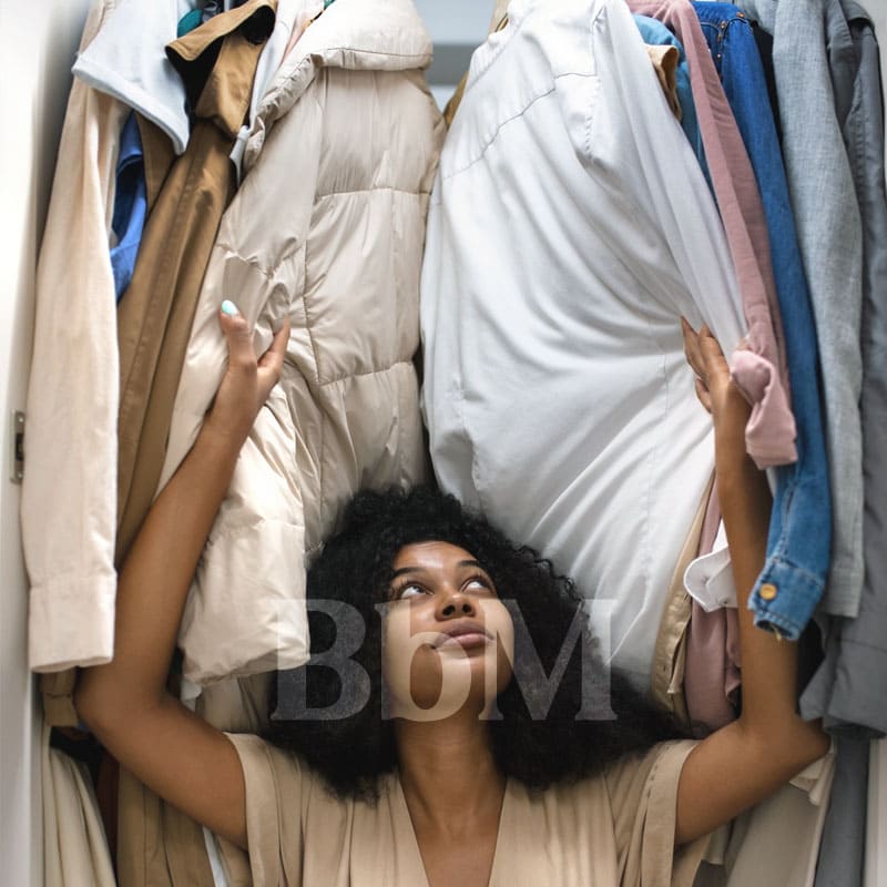dressing tri vinted vetement printemps menage femme mode bebymaman Femme faisant le tri dans un dressing encombré, entourée de vêtements d’hiver avant le rangement de printemps.