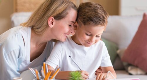 Maman souriante aidant son fils à faire ses devoirs à la maison, symbole d’éducation DIY, de complicité et d’apprentissage ludique en famille.