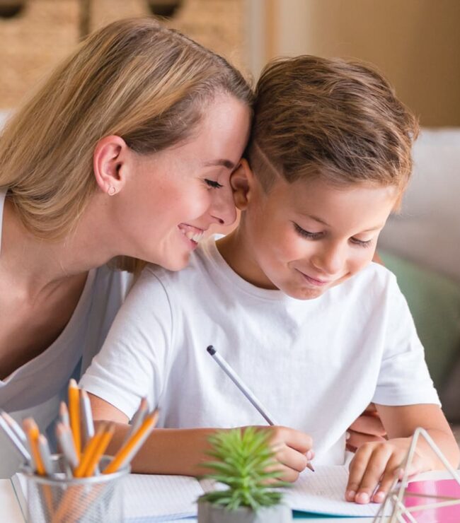 Maman souriante aidant son fils à faire ses devoirs à la maison, symbole d’éducation DIY, de complicité et d’apprentissage ludique en famille.
