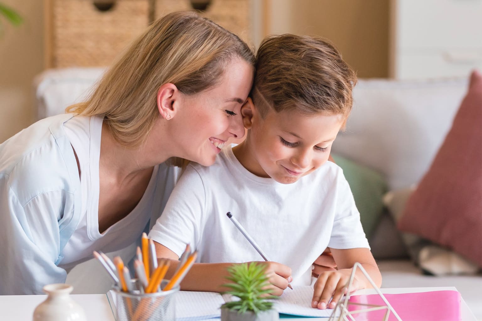 Maman souriante aidant son fils à faire ses devoirs à la maison, symbole d’éducation DIY, de complicité et d’apprentissage ludique en famille.