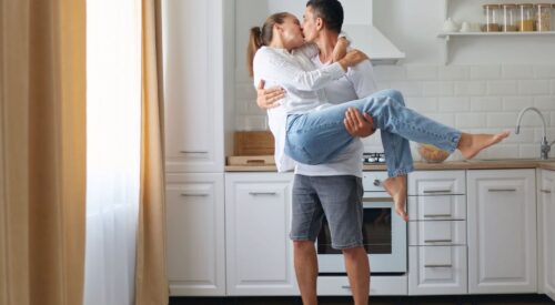 Couple de parents s’embrassant dans la cuisine, moment de complicité au quotidien
