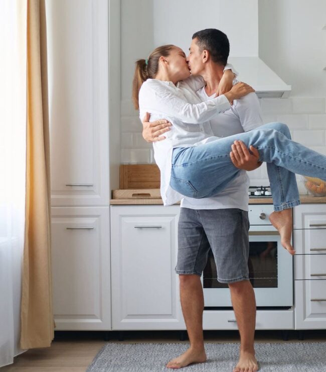Couple de parents s’embrassant dans la cuisine, moment de complicité au quotidien