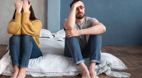 Couple en crise assis au sol dans une chambre, symbolisant une rupture et la perte d’équilibre dans la vie de couple