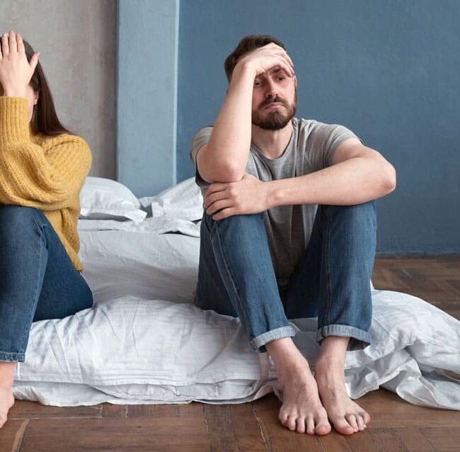 Couple en crise assis au sol dans une chambre, symbolisant une rupture et la perte d’équilibre dans la vie de couple