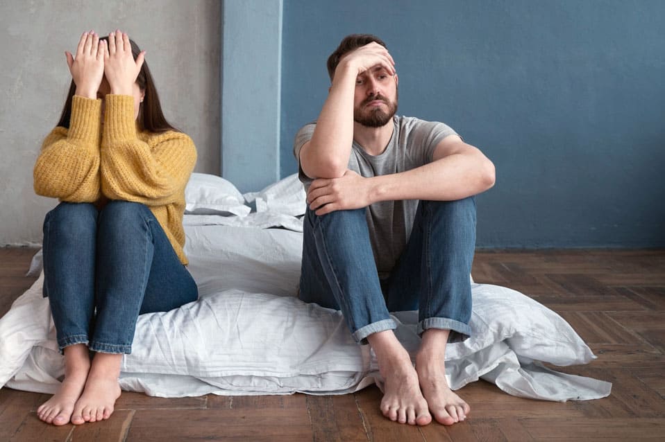 Couple en crise assis au sol dans une chambre, symbolisant une rupture et la perte d’équilibre dans la vie de couple