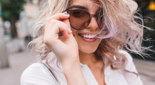 Jeune femme souriante portant des lunettes photocromiques aux verres légèrement teintés marron et monture épaisse, illustration d'un style tendance alliant confort visuel et élégance.