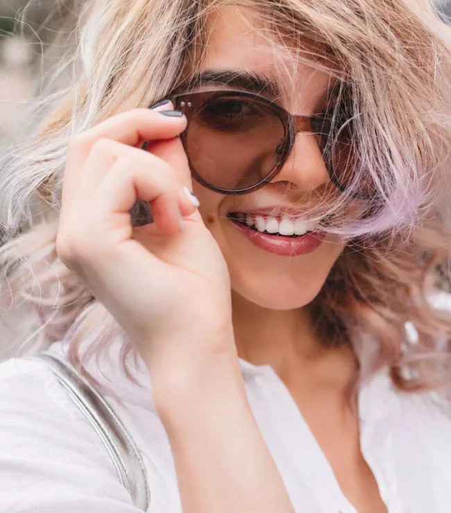 Jeune femme souriante portant des lunettes photocromiques aux verres légèrement teintés marron et monture épaisse, illustration d'un style tendance alliant confort visuel et élégance.