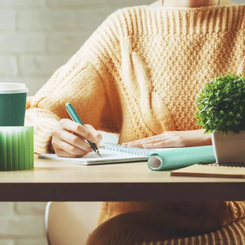maman hybride bebymaman lifestyle pourquoi Femme écrivant dans un carnet à son bureau, illustrant le quotidien d'une maman hybride qui jongle entre ses projets personnels, son travail et sa vie de famille.