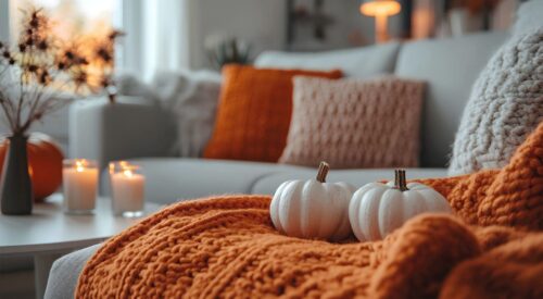 Salon cosy d’automne avec plaid orange, coussins moelleux et bougies allumées