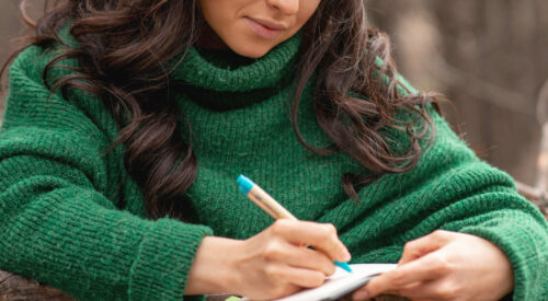 femme moderne écrivant une lettre dans un carnet, pull vert oversize, moment cocooning et introspection hivernale