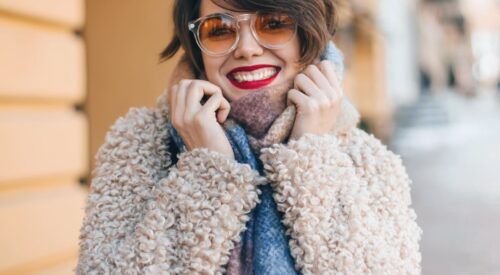 Femme souriante en look cosy chic d’automne avec manteau moumoute et écharpe colorée