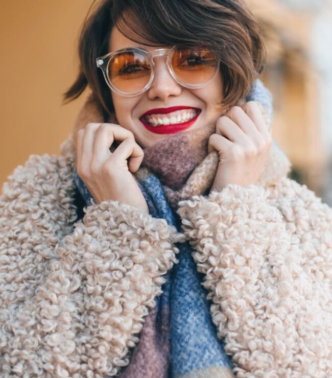 Femme souriante en look cosy chic d’automne avec manteau moumoute et écharpe colorée