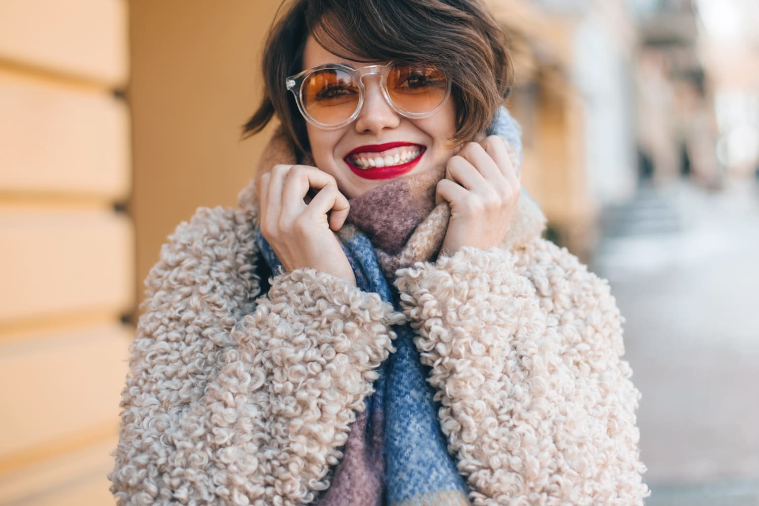 Femme souriante en look cosy chic d’automne avec manteau moumoute et écharpe colorée