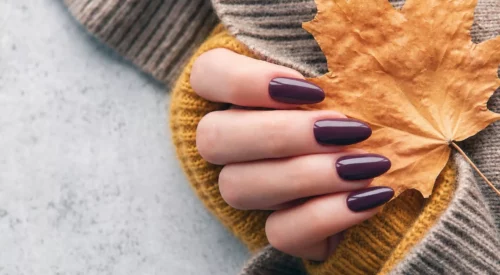 Manucure automne bordeaux brillant avec pull jaune moutarde, maille taupe et feuille d’automne