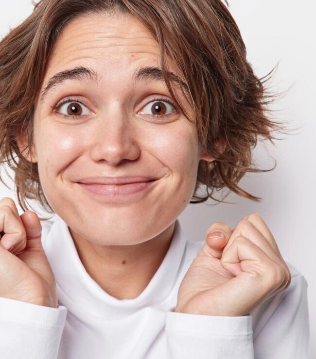 Femme naturelle souriante sans maquillage, cheveux courts, expression spontanée de bien-être et de confiance en soi.