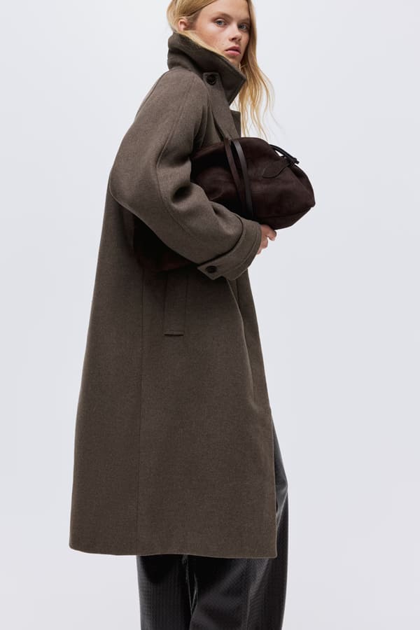 manteau long hetm hiver 2026 Femme portant un manteau long marron avec ceinture à nouer de chez H&M.