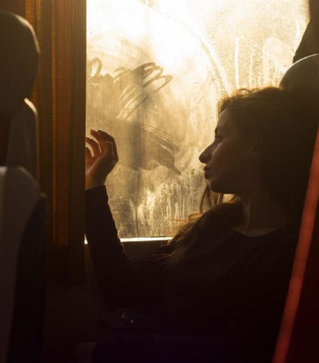silhouette d’une femme assise près d’une fenêtre de train, regard tourné vers l’extérieur, ambiance introspective