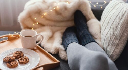 Moment cocooning d’hiver pour maman : pause bien-être sur le canapé avec plaid, café chaud et cookies, symbole de slow life, détente et temps pour soi en janvier