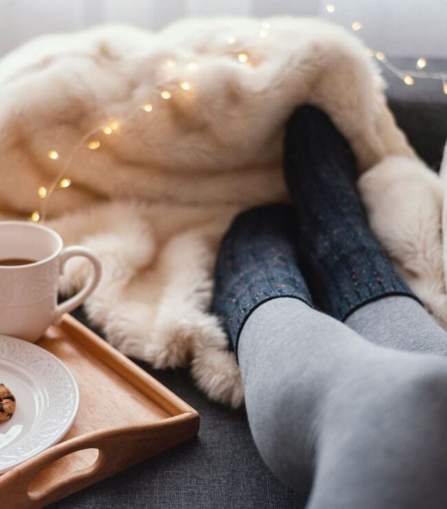 Moment cocooning d’hiver pour maman : pause bien-être sur le canapé avec plaid, café chaud et cookies, symbole de slow life, détente et temps pour soi en janvier