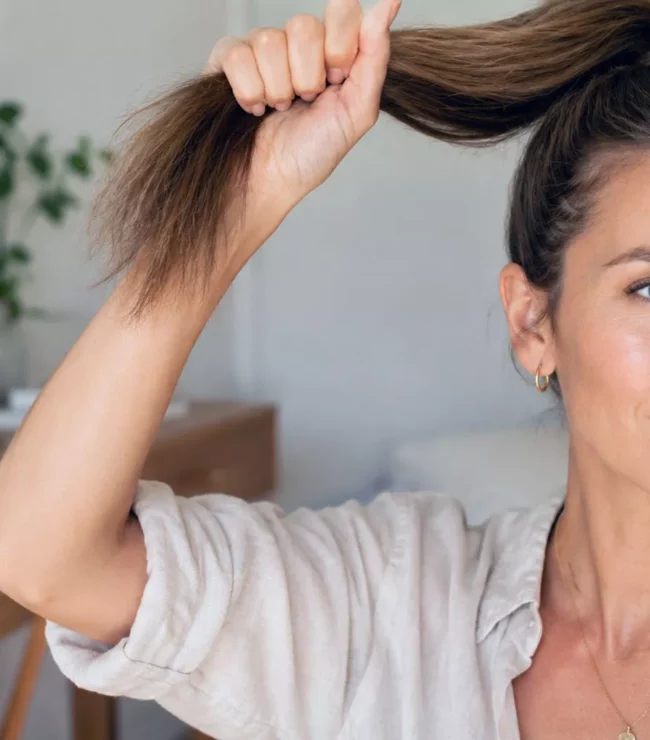 Femme aux cheveux fins châtain clair tenant sa queue-de-cheval dans un intérieur naturel et lumineux