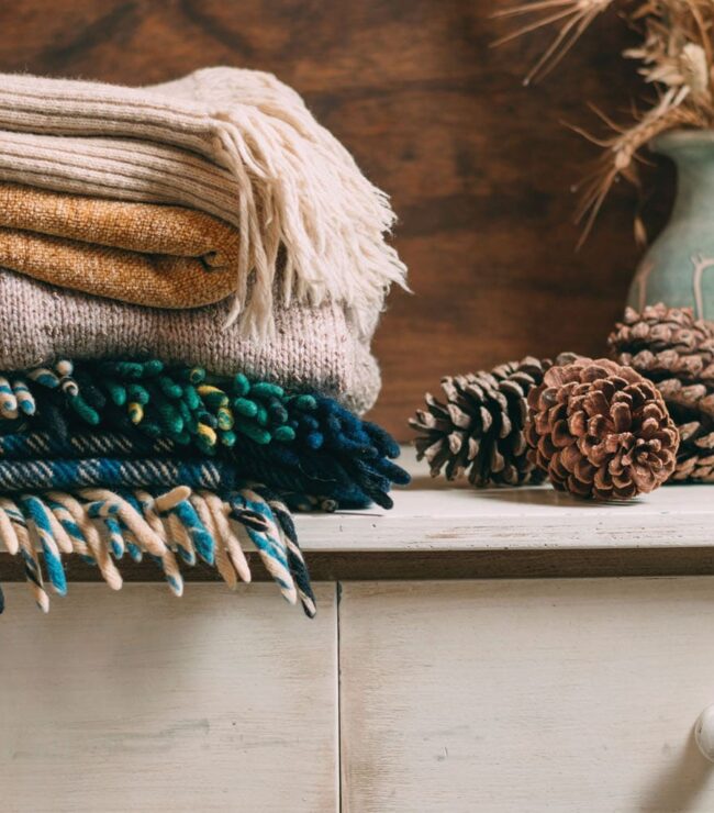 Plaids et tricots d’hiver pliés dans des tons chauds, ambiance cosy et cocooning.