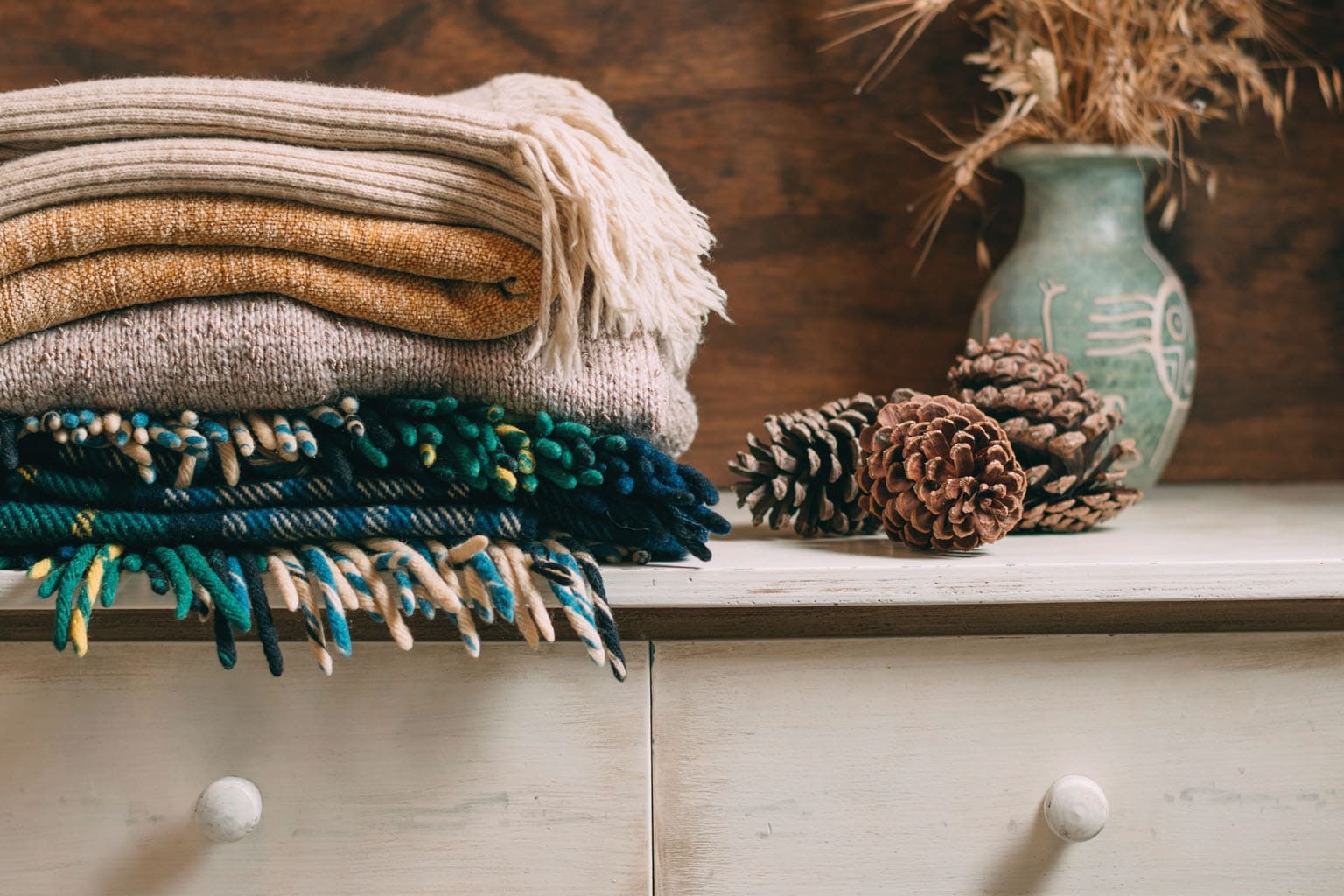Plaids et tricots d’hiver pliés dans des tons chauds, ambiance cosy et cocooning.