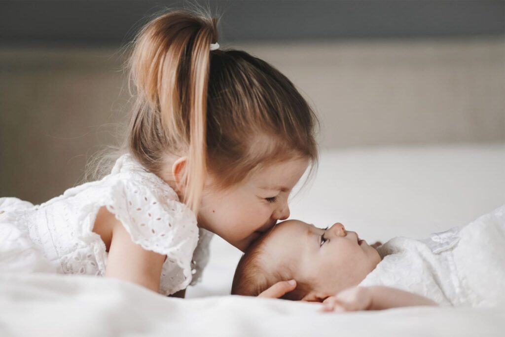 fratrie enfants famille fille garcon amour fraternel frere et soeur bebymaman Grande sœur embrassant tendrement son petit frère allongé, moment de douceur entre fratrie.