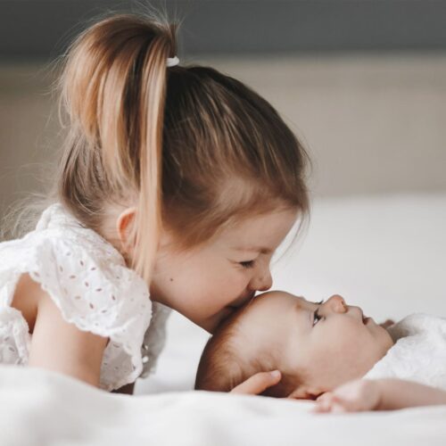 fratrie enfants famille fille garcon amour fraternel frere et soeur bebymaman Grande sœur embrassant tendrement son petit frère allongé, moment de douceur entre fratrie.