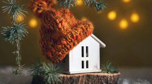 Maison miniature en hiver avec bonnet tricoté orange, symbole de slow home et de cocooning familial.