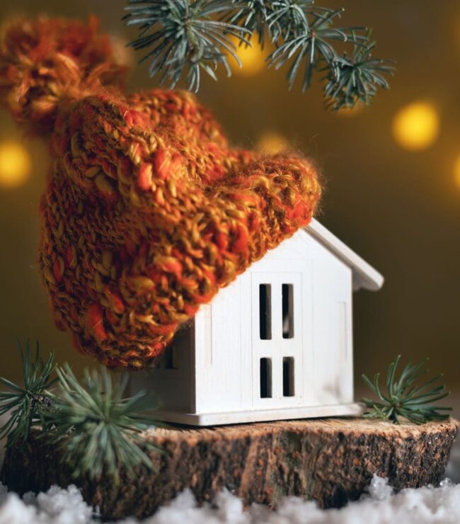 Maison miniature en hiver avec bonnet tricoté orange, symbole de slow home et de cocooning familial.