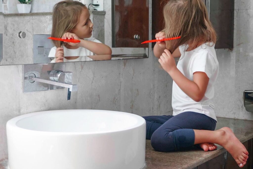 routine famille enfant participer preparation collectif fille se coiffe bebymama Enfant se coiffant seule dans la salle de bain, symbole d’autonomie et de routine familiale au quotidien