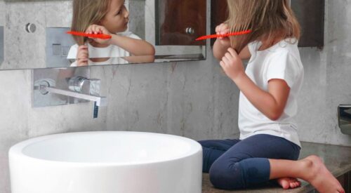 Enfant se coiffant seule dans la salle de bain, symbole d’autonomie et de routine familiale au quotidien