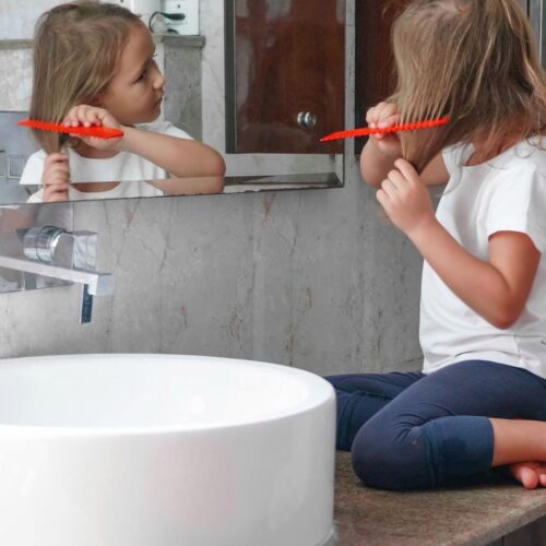 routine famille enfant participer preparation collectif fille se coiffe bebymama Enfant se coiffant seule dans la salle de bain, symbole d’autonomie et de routine familiale au quotidien