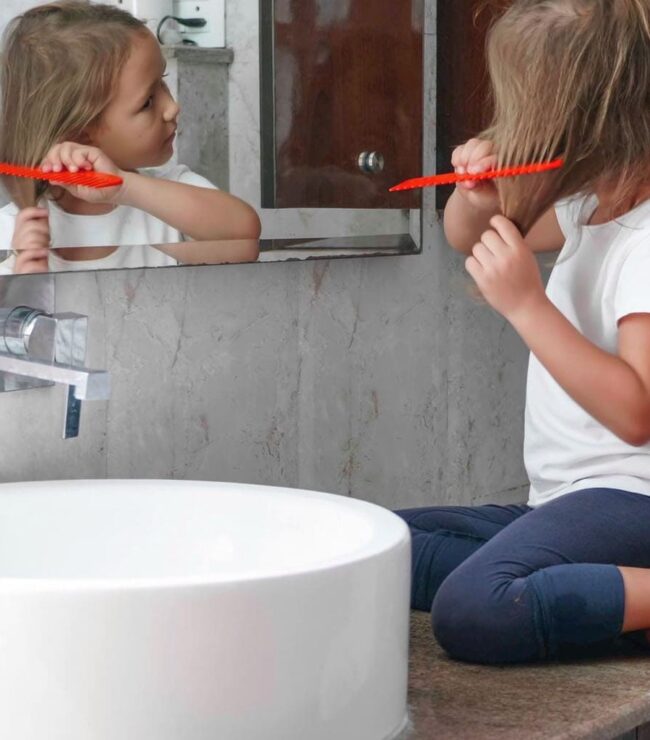 Enfant se coiffant seule dans la salle de bain, symbole d’autonomie et de routine familiale au quotidien