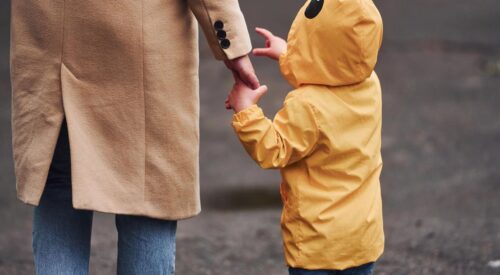 Parent tenant la main de son enfant en manteau jaune, symbole de lien parental et de parentalité bienveillante