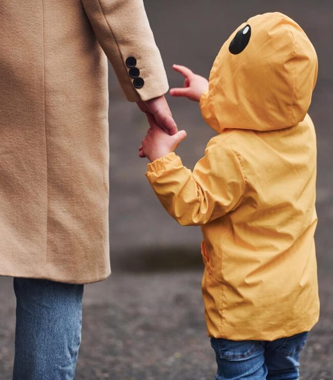 Parent tenant la main de son enfant en manteau jaune, symbole de lien parental et de parentalité bienveillante