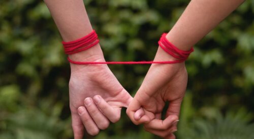 Deux mains reliées par un fil rouge, symbole d’une relation grise et d’une dépendance émotionnelle