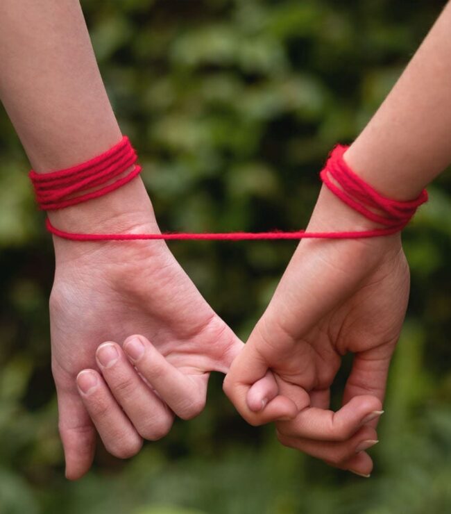 Deux mains reliées par un fil rouge, symbole d’une relation grise et d’une dépendance émotionnelle