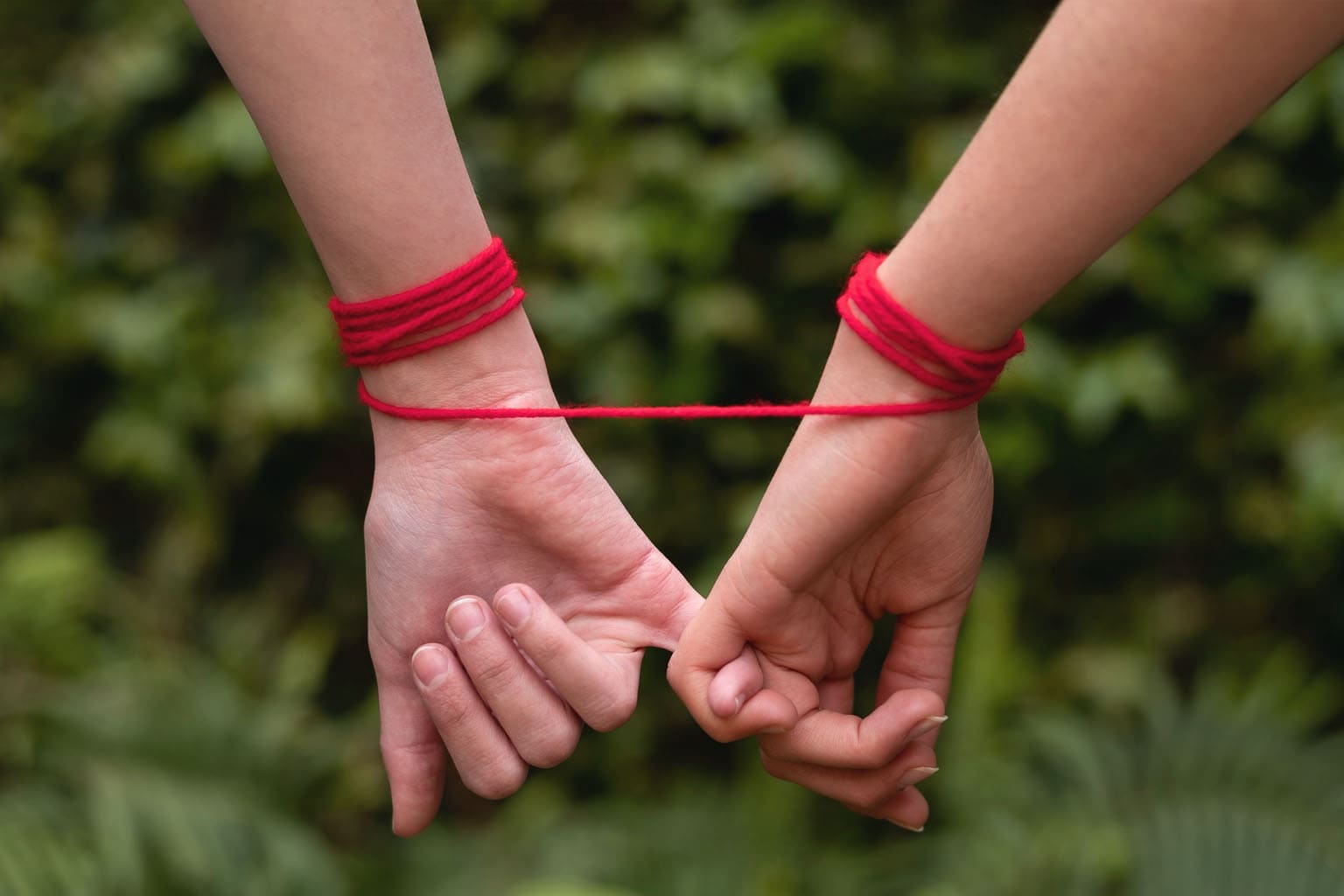 Deux mains reliées par un fil rouge, symbole d’une relation grise et d’une dépendance émotionnelle