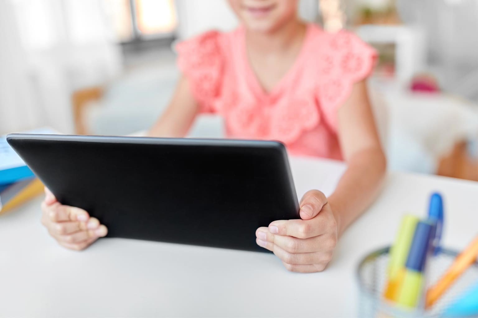 Enfant utilisant une tablette numérique à l’école, assise à un bureau avec des fournitures scolaires, symbole de la scolarité connectée et des écrans en classe.