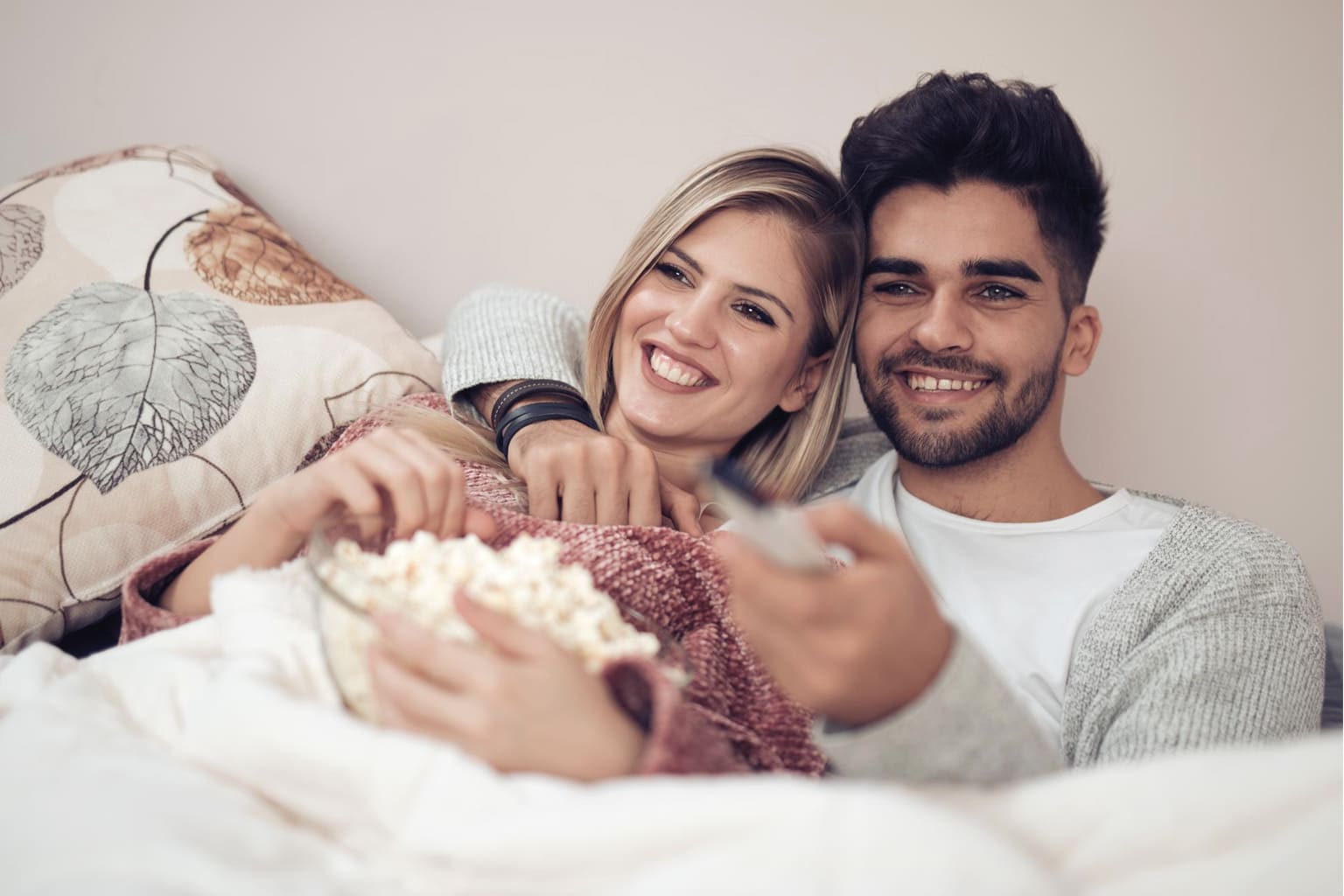 Couple souriant allongé dans un lit regardant la télévision, moment de détente et de complicité dans la chambre parentale