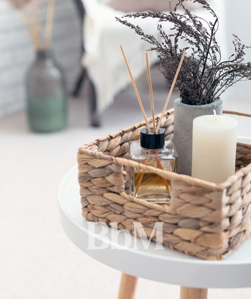 deco sensorielle encens maison printemps goodvibes bebymaman Détail déco printanier avec diffuseur de parfum, bougie blanche et fleurs séchées dans un panier en fibres naturelles posé sur une table d’appoint.